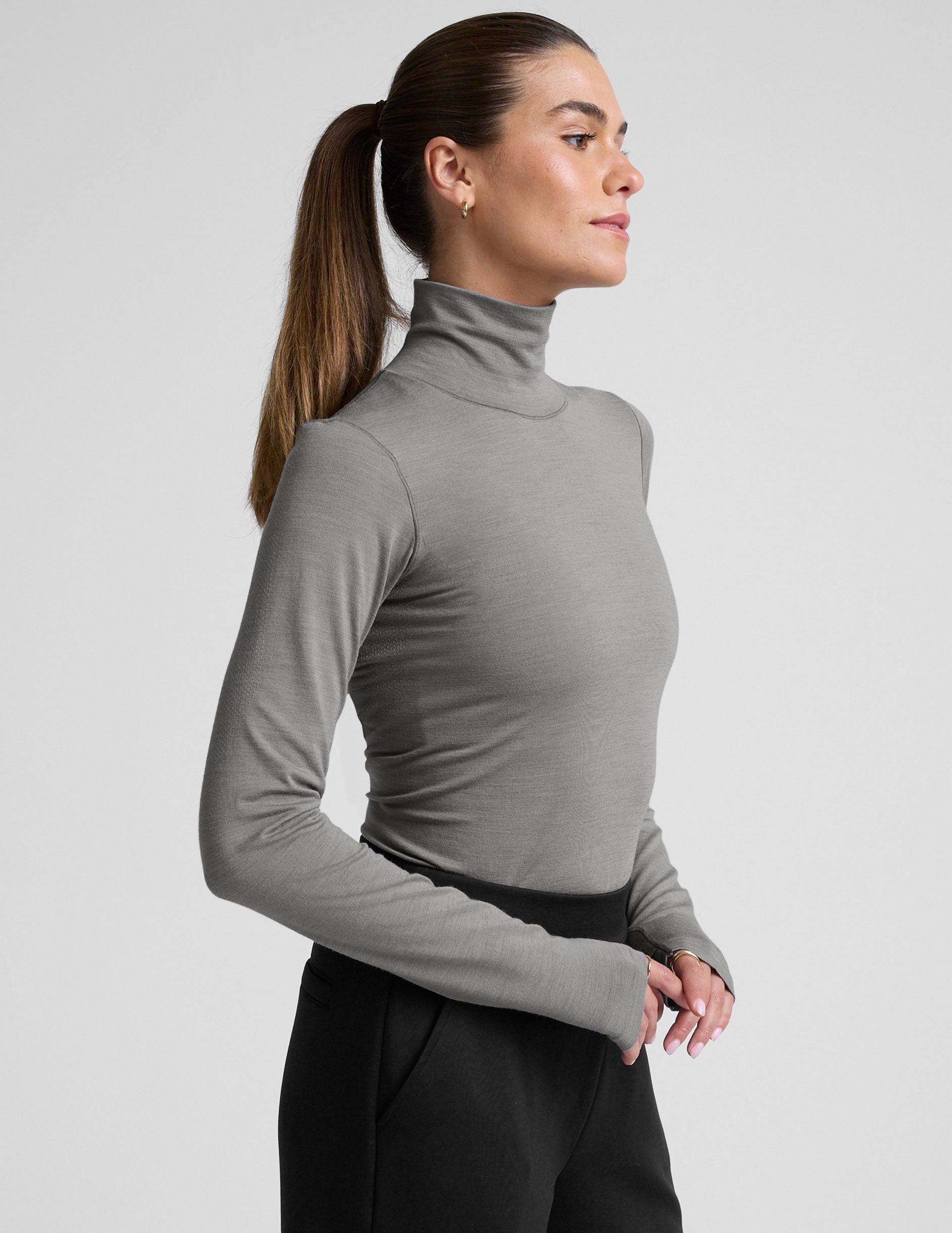 model wearing a gray turtleneck and black pants against a plain background.