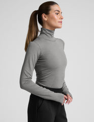 model wearing a gray turtleneck and black pants against a plain background.