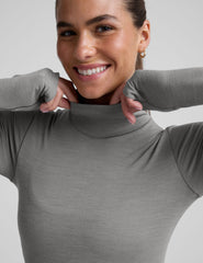 model wearing a gray turtleneck and black pants against a plain background.