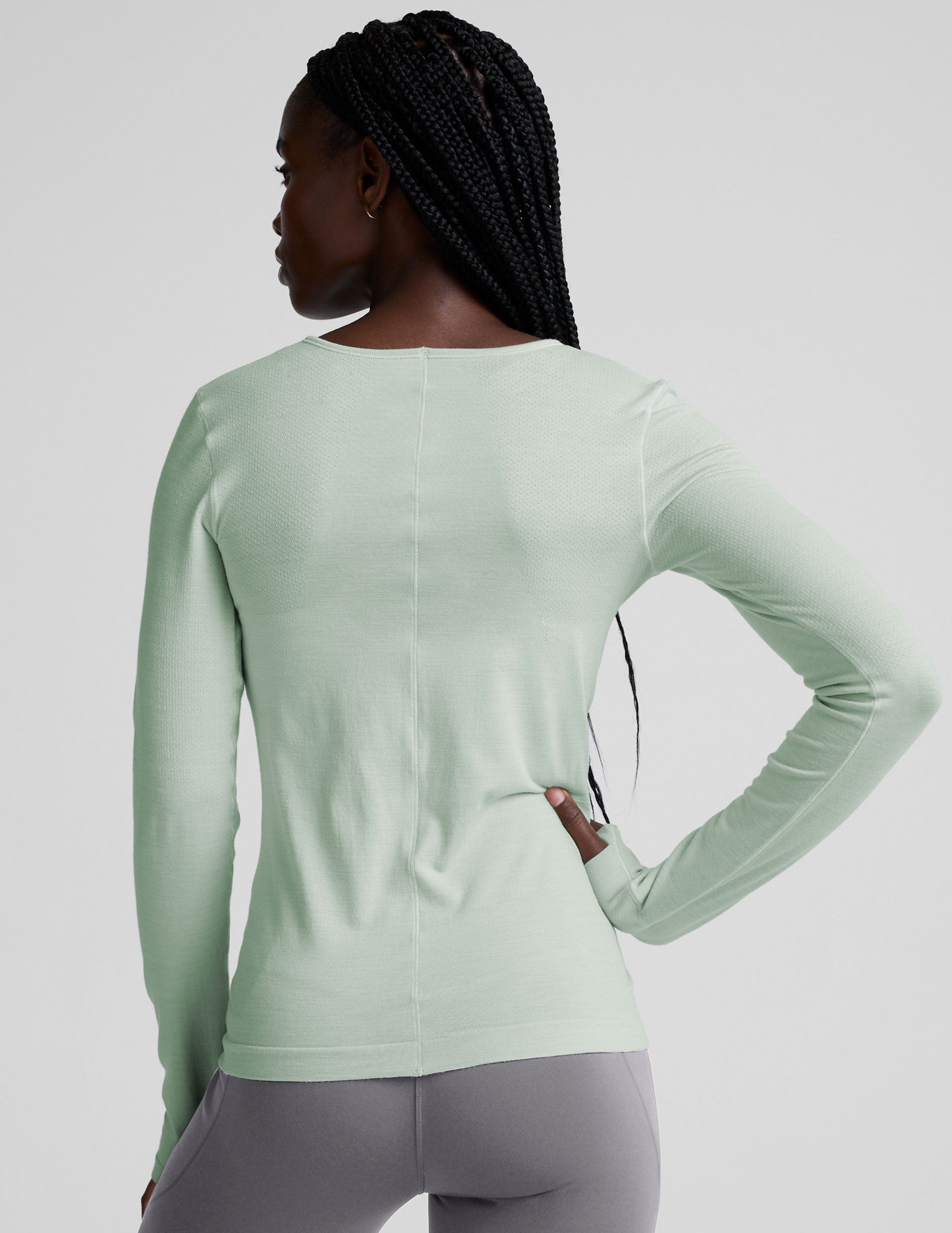 model wearing a light green long-sleeve crewneck top and gray leggings on a plain background.