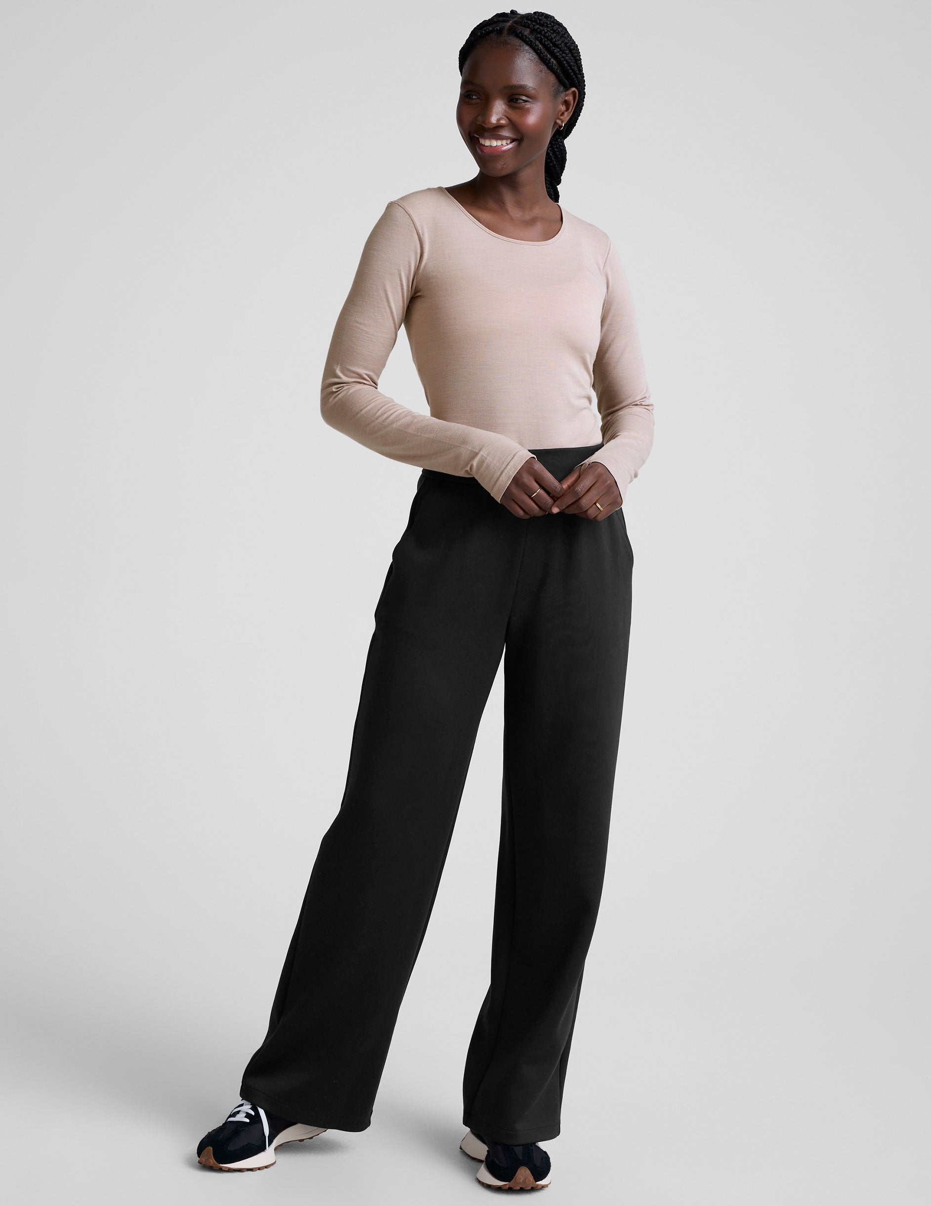 model wearing a beige long-sleeve crewneck top and black pants on a plain background.