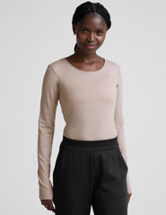 model wearing a beige long-sleeve crewneck top and black pants on a plain background.