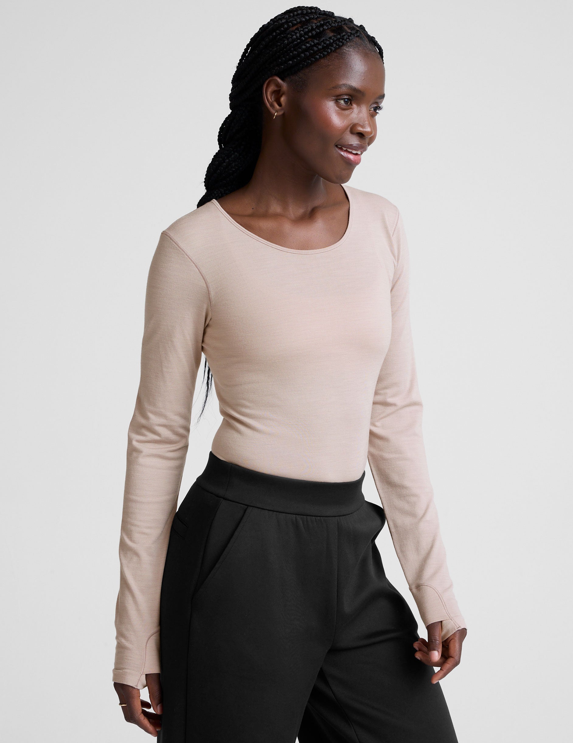 model wearing a beige long-sleeve crewneck top and black pants on a plain background.