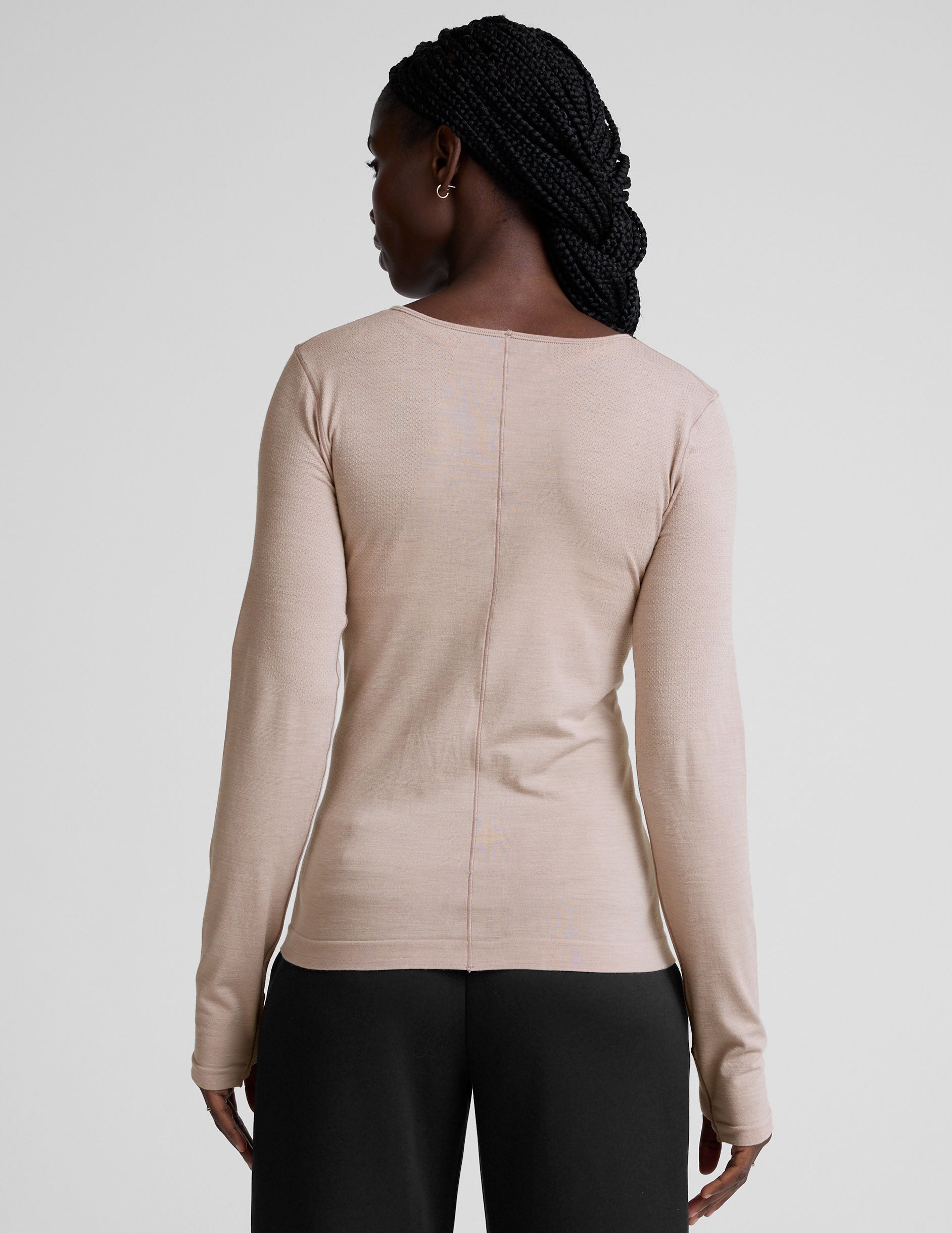 model wearing a beige long-sleeve crewneck top and black pants on a plain background.