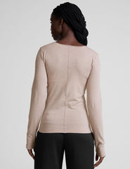 model wearing a beige long-sleeve crewneck top and black pants on a plain background.