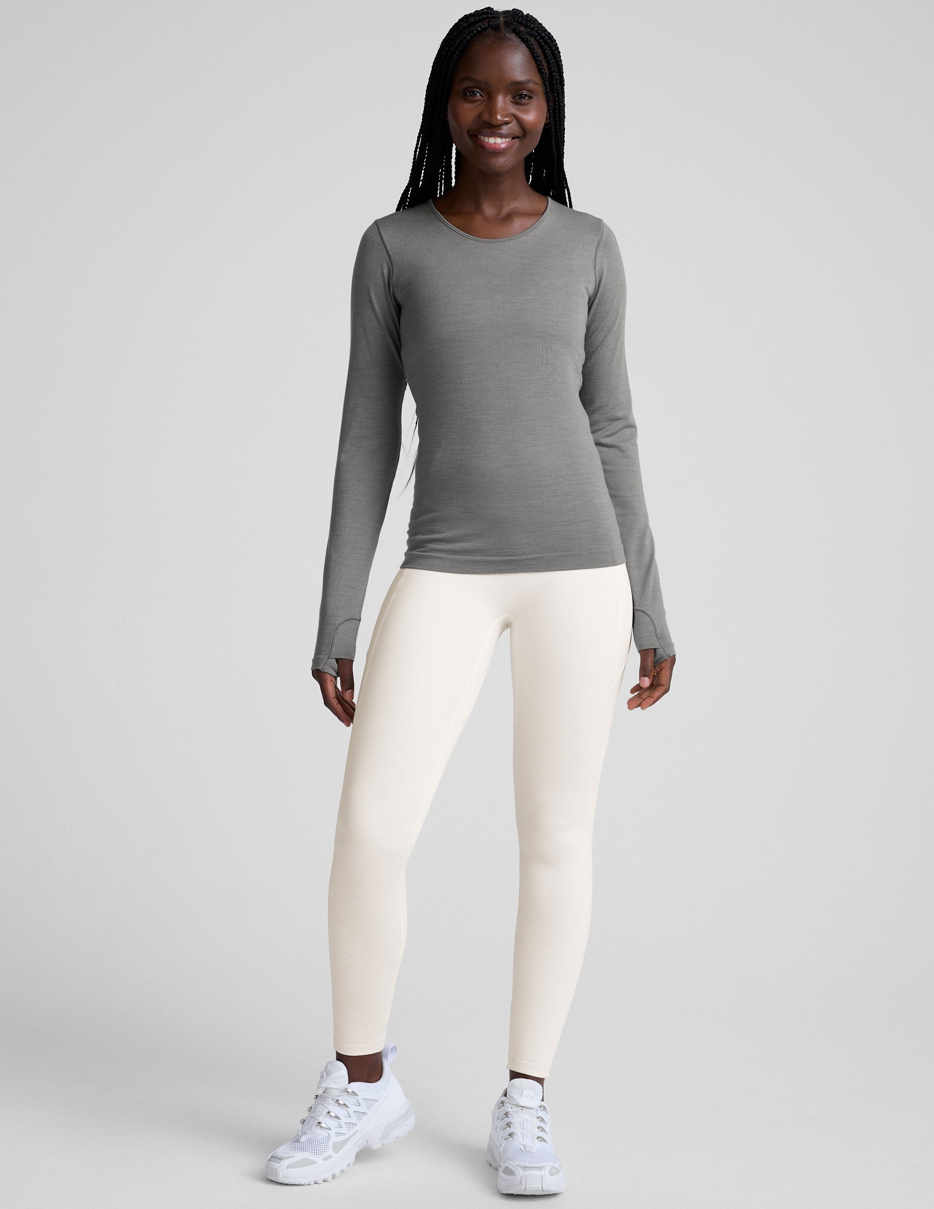 model wearing a gray long-sleeve crewneck top and white pants on a plain background.