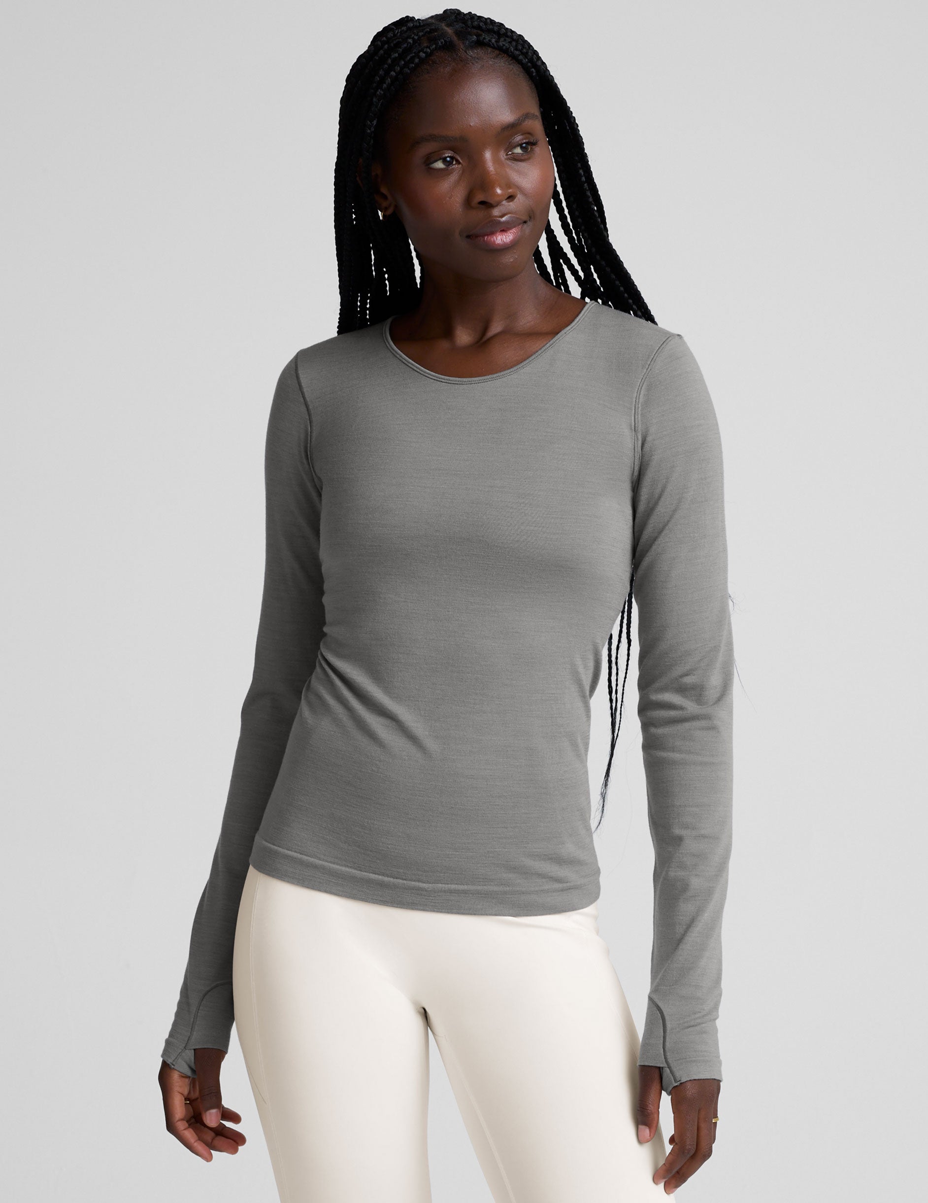 model wearing a gray long-sleeve crewneck top and white pants on a plain background.